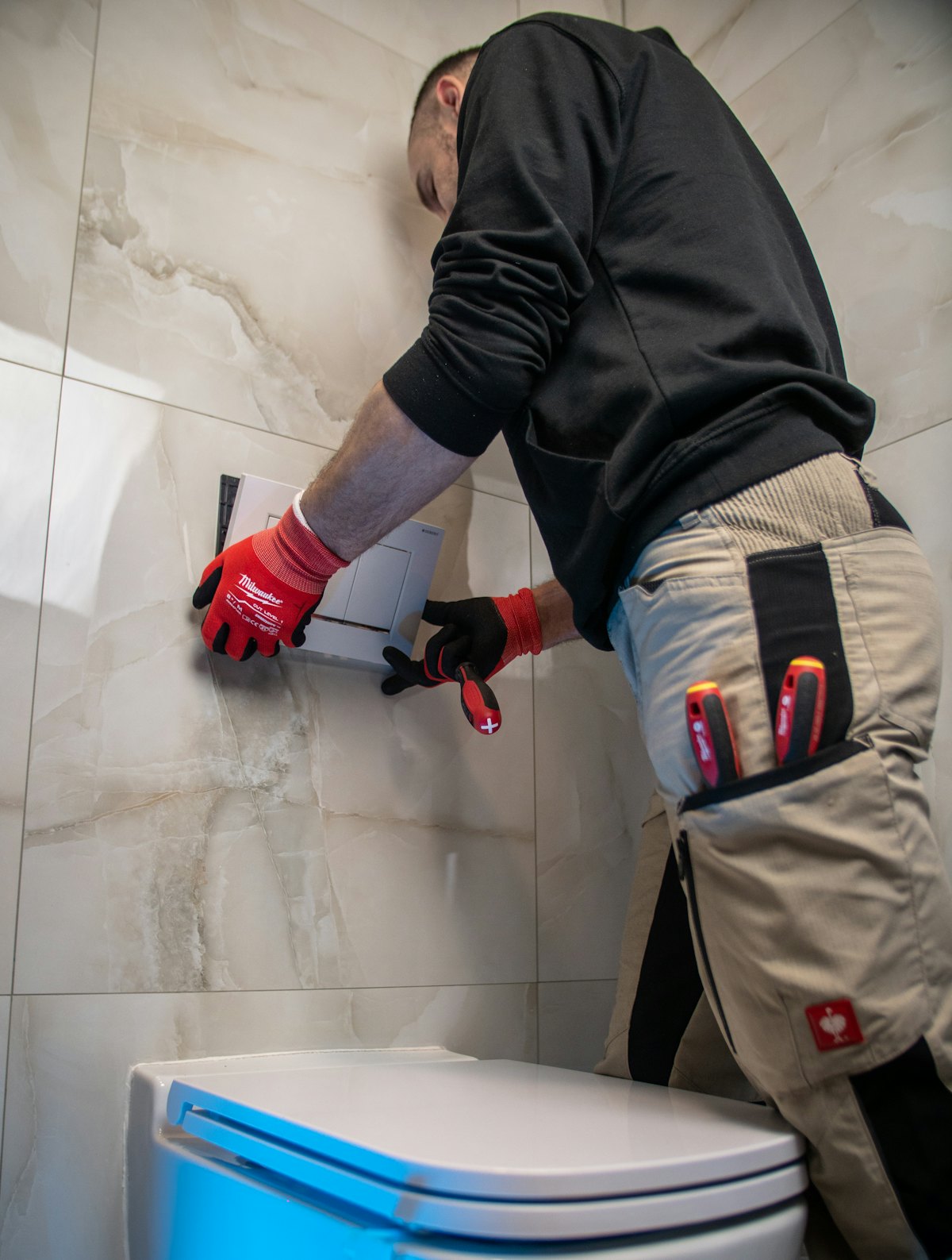 A fitter installing a flush plate above a wall-hung toilet