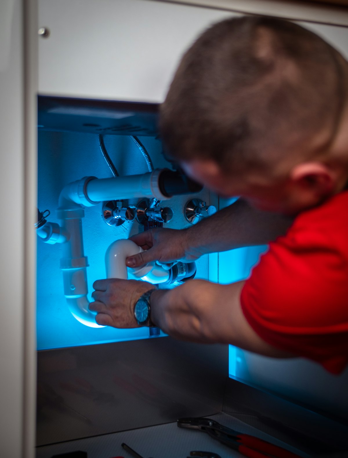 A plumber repairing the waste pipe under a basin